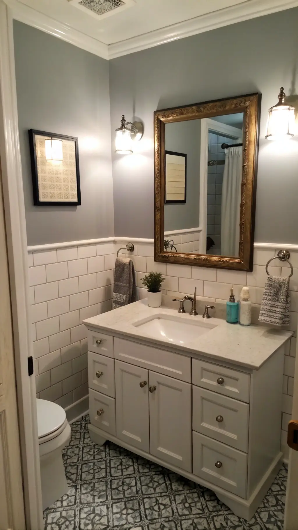 Budget-friendly bathroom makeover with light gray walls, original subway tiles, brushed nickel hardware, modern sconces, and a vintage mirror with a refreshed frame. Dramatic dusk lighting enhances the transformation.