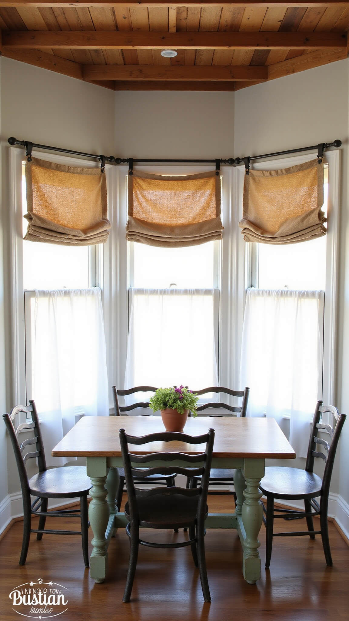 Cozy breakfast nook with triple windows, layered burlap and cotton curtains, exposed wooden beams, vintage table and ladder-back chairs, softly lit by morning light.