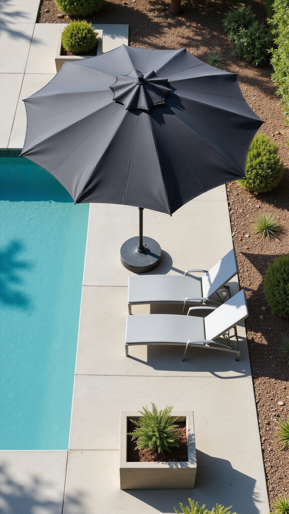 Drone view of a modern poolside retreat featuring a large charcoal cantilever umbrella, turquoise pool, sleek grey chaise lounges, and geometric planters with succulents, all casting strong midday shadows.