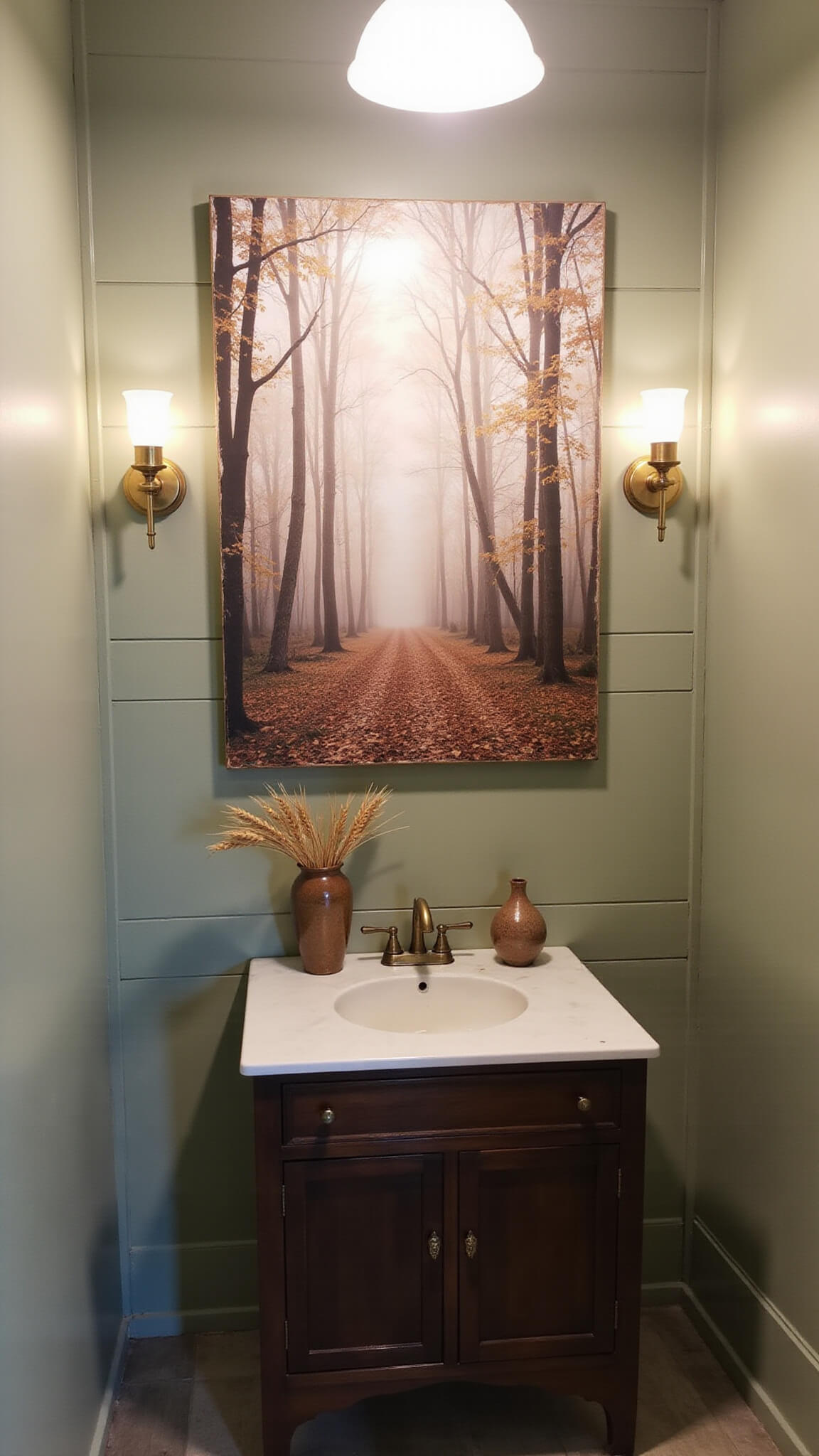 Intimate powder room with sage green shiplap walls, sepia forest photograph, brass sconces, and dark wood vanity with ceramic vessels of dried wheat.