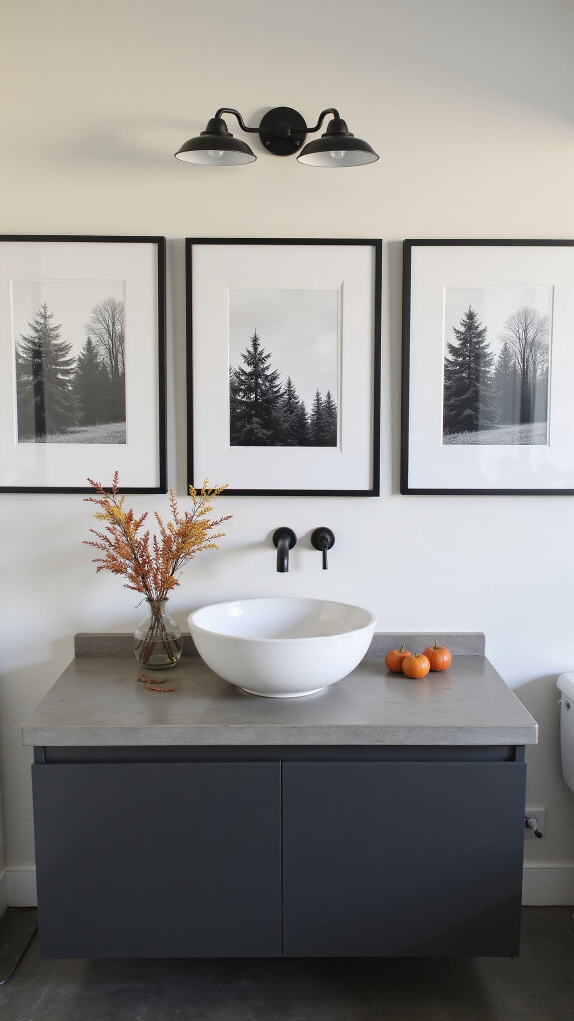 Minimalist 7x8ft guest bathroom with floating vanity, black and white autumn landscape prints above, concrete countertop, matte black accessories, and a fall foliage branch under soft afternoon light.