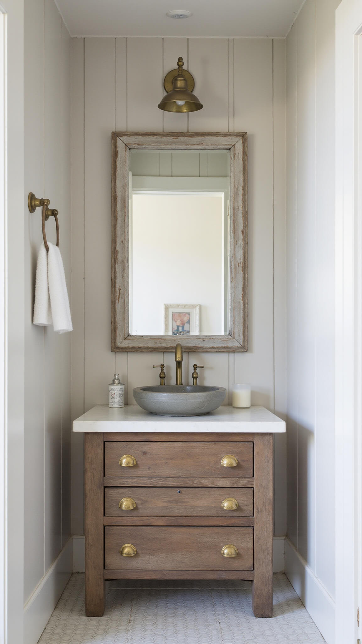 Charming greige powder room with board and batten walls, salvaged window mirror, concrete vessel sink on weathered wood vanity, and brass hardware.