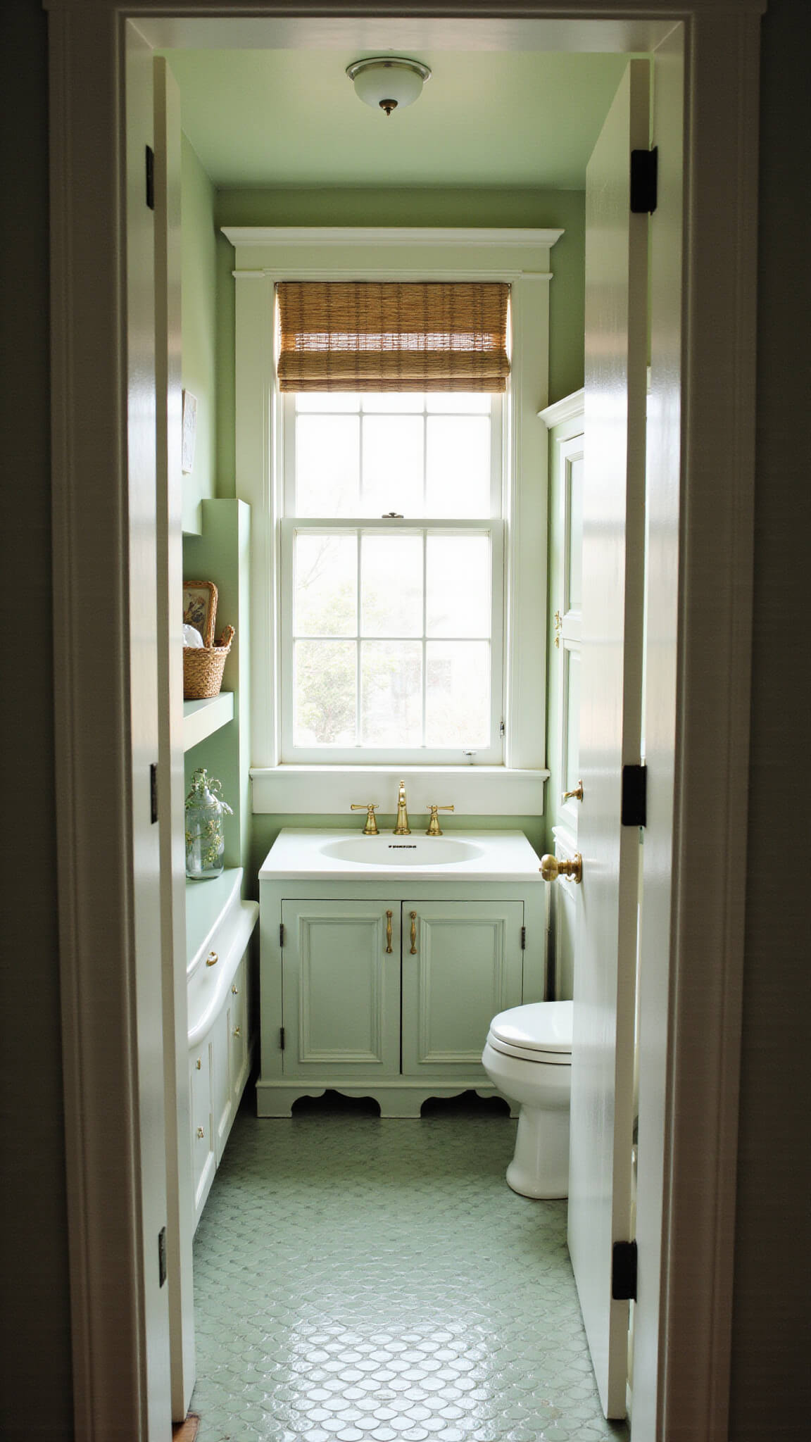 Cozy 5x8ft white bathroom with sage green ceiling, built-in linen cabinet, pedestal sink with brass faucet, sage green penny tile floor, and woven roman shade.