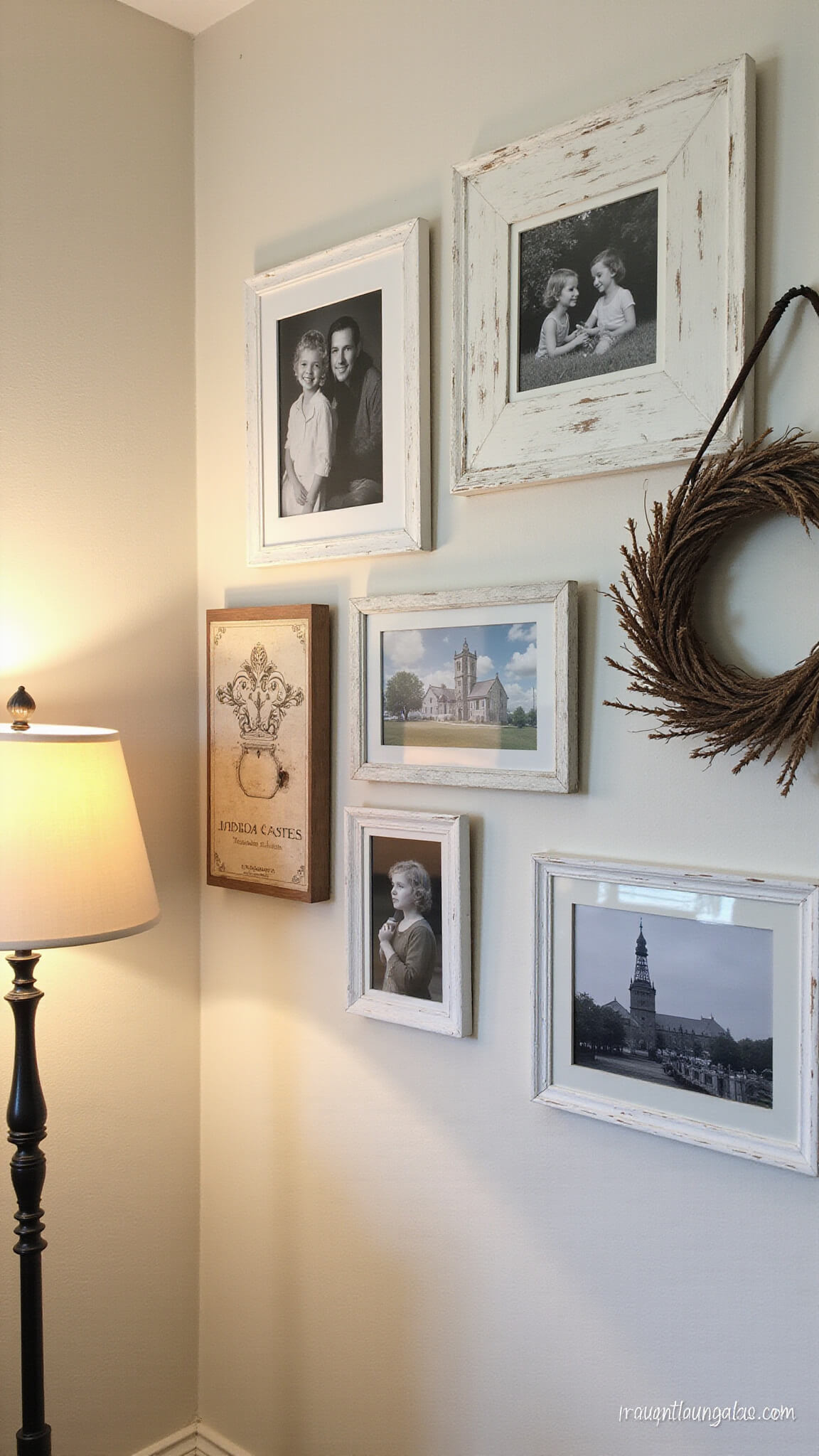 Farmhouse gallery wall vignette at dusk with black and white photos in distressed white frames, vintage salvage pieces, and cotton wreath under warm lamp lighting on creamy white walls.