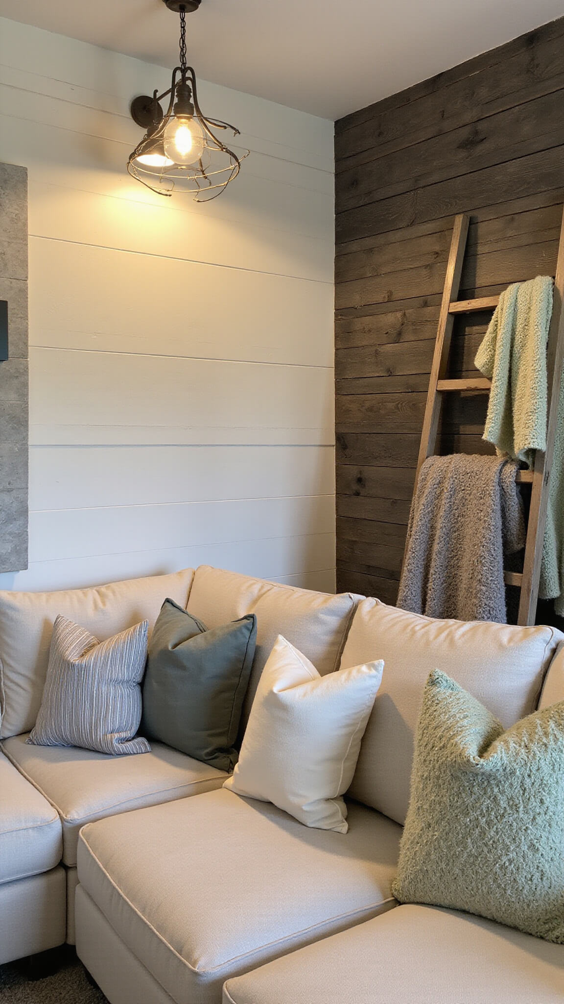 Cozy 16x20ft corner room at dusk with vintage wall sconces and iron chandelier, featuring Alabaster White shiplap, dark wood accent wall, linen sectional with textured pillows, and antique ladder with knit throws.