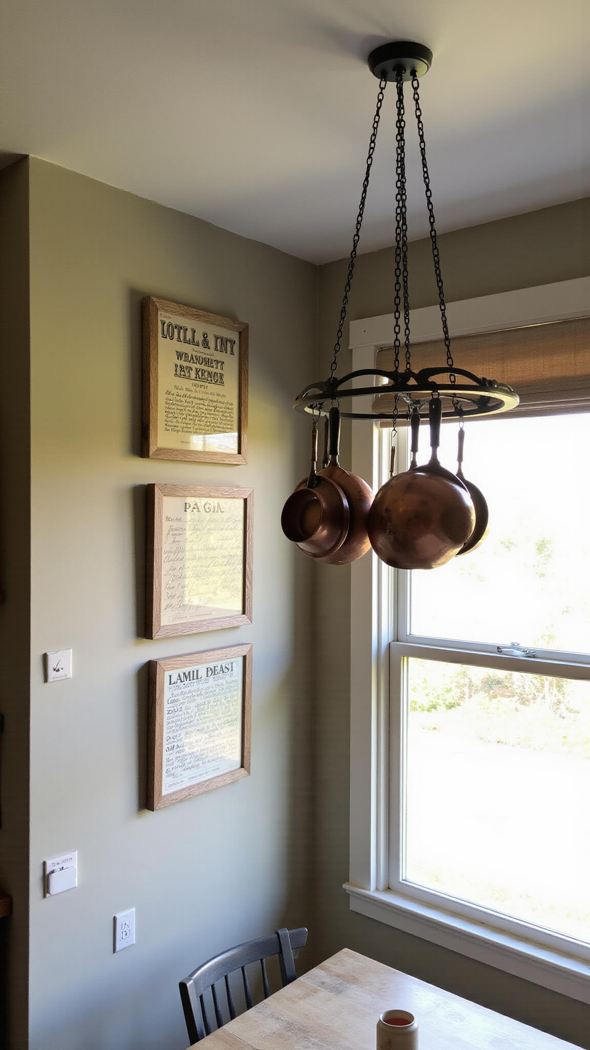Cozy breakfast nook with 9ft ceiling, vintage crate label and recipe gallery wall, copper cookware on wrought iron rack, and soft light through linen roman shade.