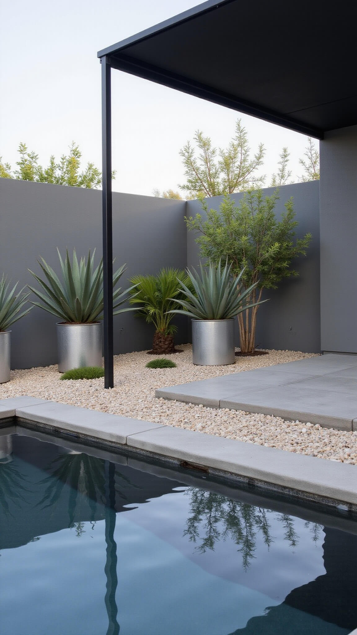 Modern poolside garden room with zero-edge dark gray pool reflecting minimalist shade structure, floating concrete pavers, and sculptural agaves and aloes in metallic planters at midday.