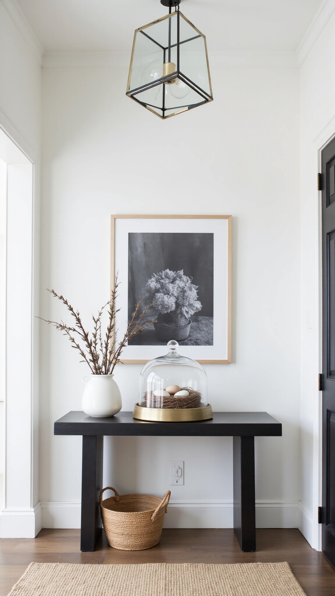 Minimalist Easter foyer with tall ceilings, geometric pendant light, console table featuring glass cloche and nest, large black and white botanical print, and pussy willow arrangement in woven basket.