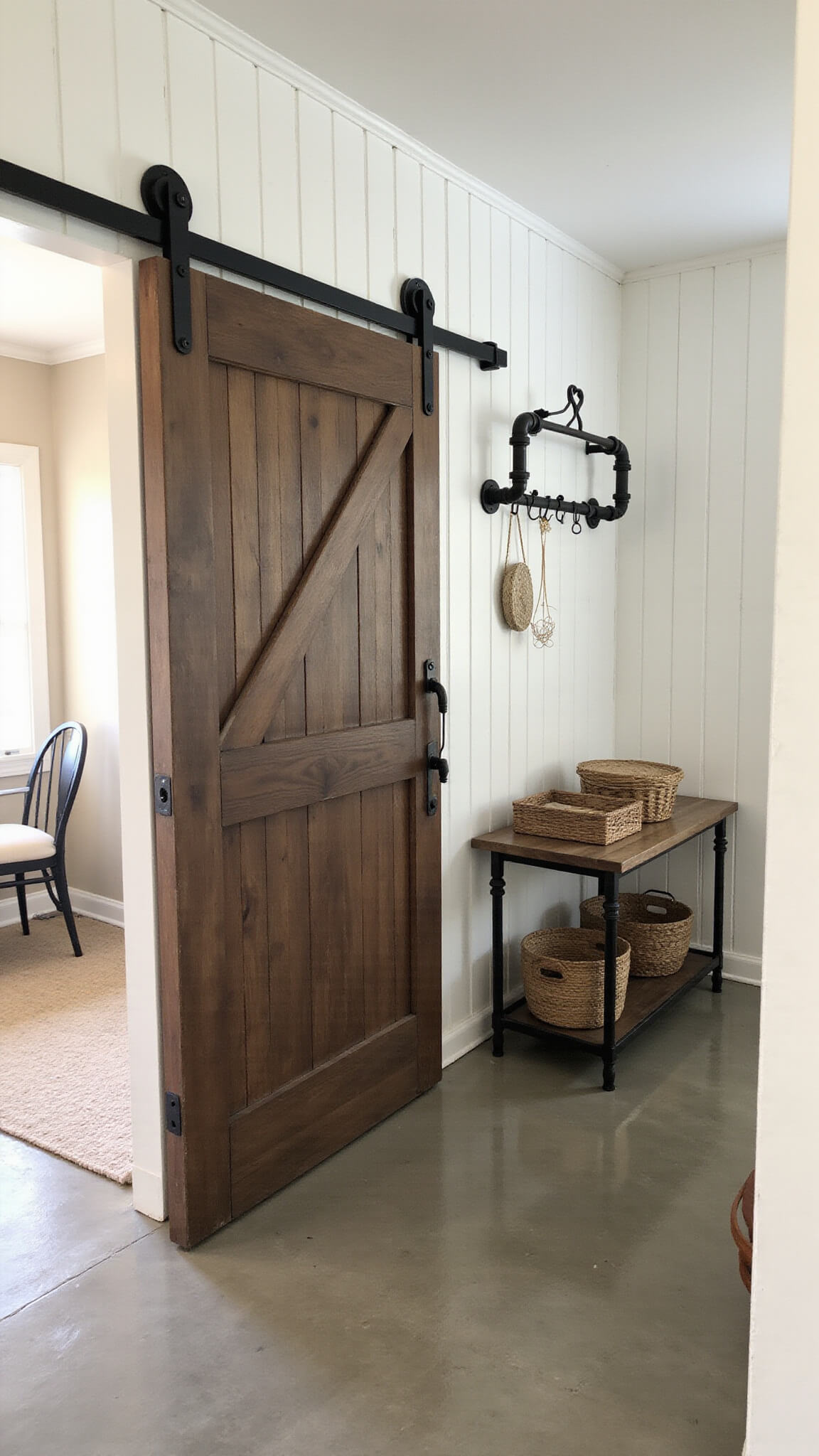 Industrial-style entryway with sliding barn door, concrete floors, shiplap walls, vintage cart console, pipe coat rack, and woven basket decor in morning light.