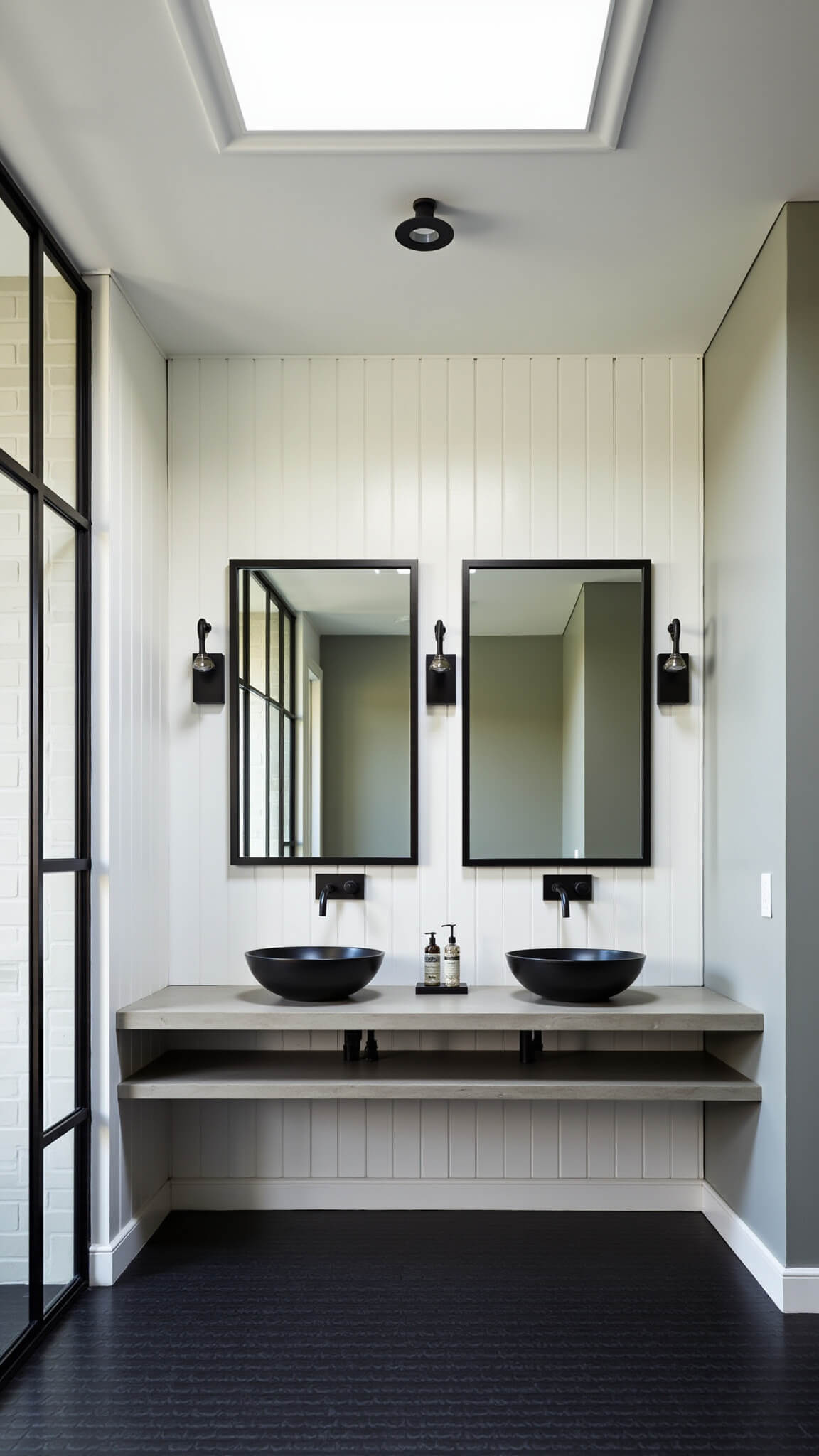 Modern barn bathroom with concrete floating vanity, vessel sinks, black-framed mirrors, industrial sconces, black hex tile floor, and skylight-lit shower with steel frame glass enclosure.