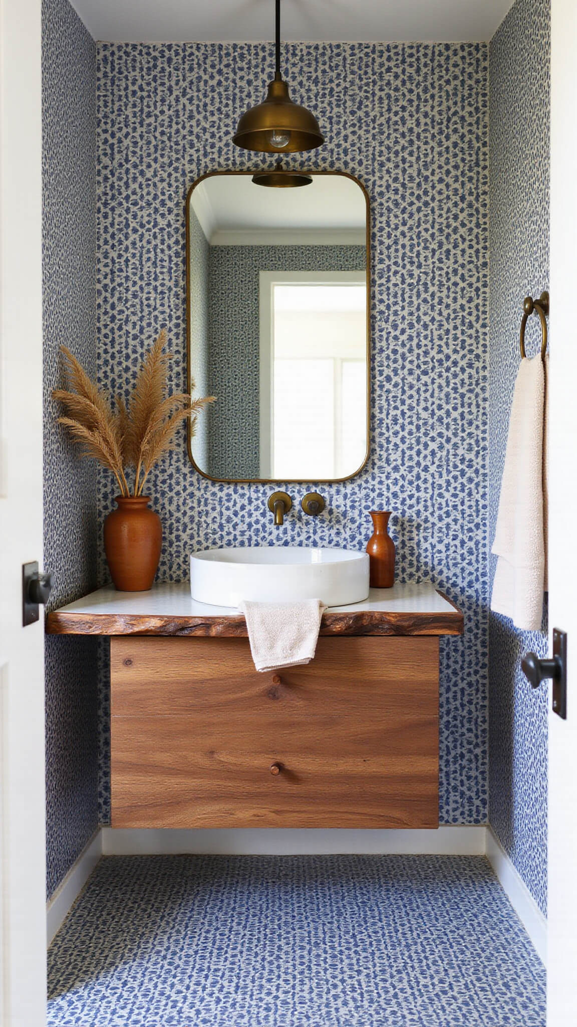 Midday view of a stylish powder room with navy and white geometric tile feature wall, floating walnut vanity, white vessel sink, brass mirror and pendant, and natural decor accents.